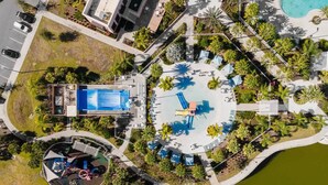 Vista aérea de um resort com piscina, espreguiçadeiras e um elemento aquático circular.