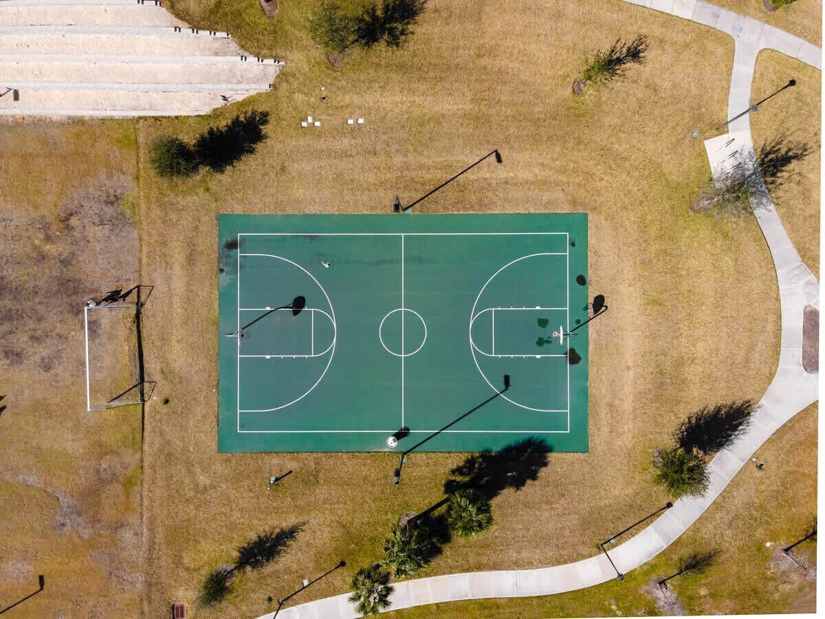 An aerial view of a basketball court with surrounding grassy areas and pathways.