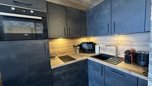 Une cuisine moderne avec des meubles de couleur sombre, un four encastré, un évier et un four à micro-ondes.