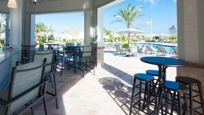 A spacious outdoor patio with multiple seating areas, including tables and chairs, overlooking a pool area with umbrellas and lounge chairs.