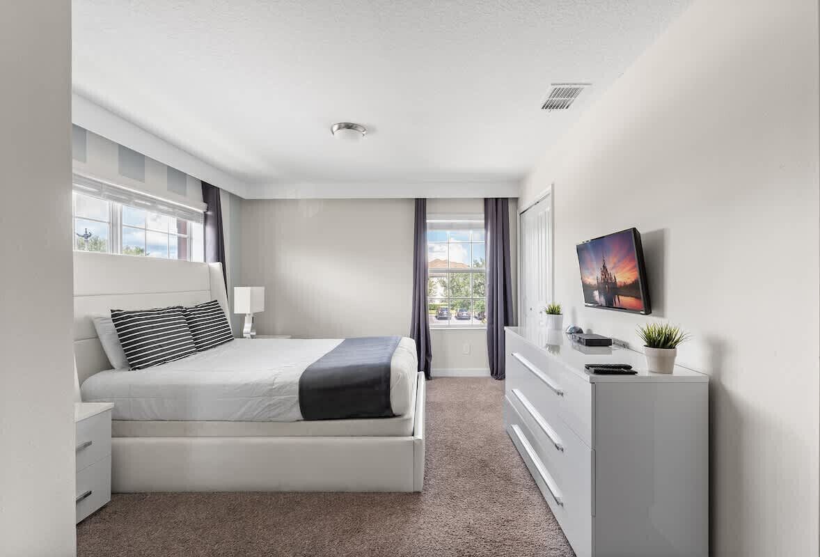 A modern bedroom with a bed, dresser, and a TV mounted on the wall.