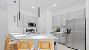 A modern kitchen with white cabinetry, stainless steel appliances, and a central island with two wooden chairs.