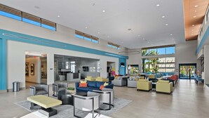 A spacious lobby with multiple seating areas, a kitchen in the background, and large windows providing natural light.