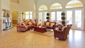 A spacious lobby with a large sectional sofa, a coffee table, and a fireplace. There are large windows with arched tops and a reception desk with a plant. - Disney Getaway! Private Pool & Game Room. Book Now! #BV77 (Orlando)