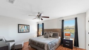 A bedroom with a bed, a ceiling fan, a nightstand, a chair, and a window with curtains.