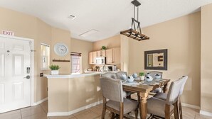 A dining area with a wooden table and chairs, a kitchen in the background, and an exit door. - Disney Getaway! Townhouse with Private Pool. Book Now! #EIR68 (Orlando)