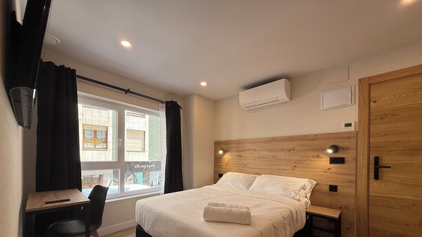 A bedroom with a bed, bedside table, chair, and a window with curtains.