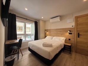 A bedroom with a bed, bedside table, chair, and a window with curtains. - CC Gijon (Gijón)