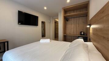 Una habitación de hotel con una cama grande, un televisor montado, un armario de madera y una mesita de noche.
