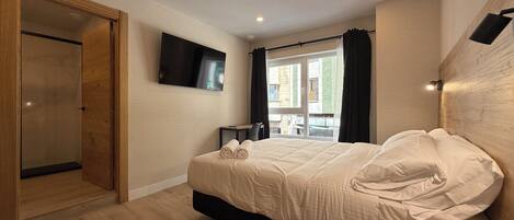 Una habitación de hotel moderna con una cama grande, un televisor de pantalla plana montado en la pared y vistas al exterior a través de una ventana.