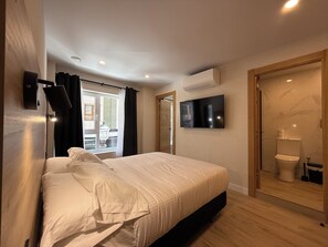 A bedroom with a bed, a TV mounted on the wall, an air conditioning unit, and a wooden door leading to a bathroom. - CC Gijon (Gijón)