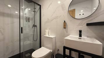 Un baño moderno con ducha de vidrio, inodoro, lavamanos y espejo.