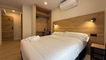 Una habitación de hotel moderna con una cama grande, cabecero de madera, armario empotrado y aire acondicionado instalado en la pared.
