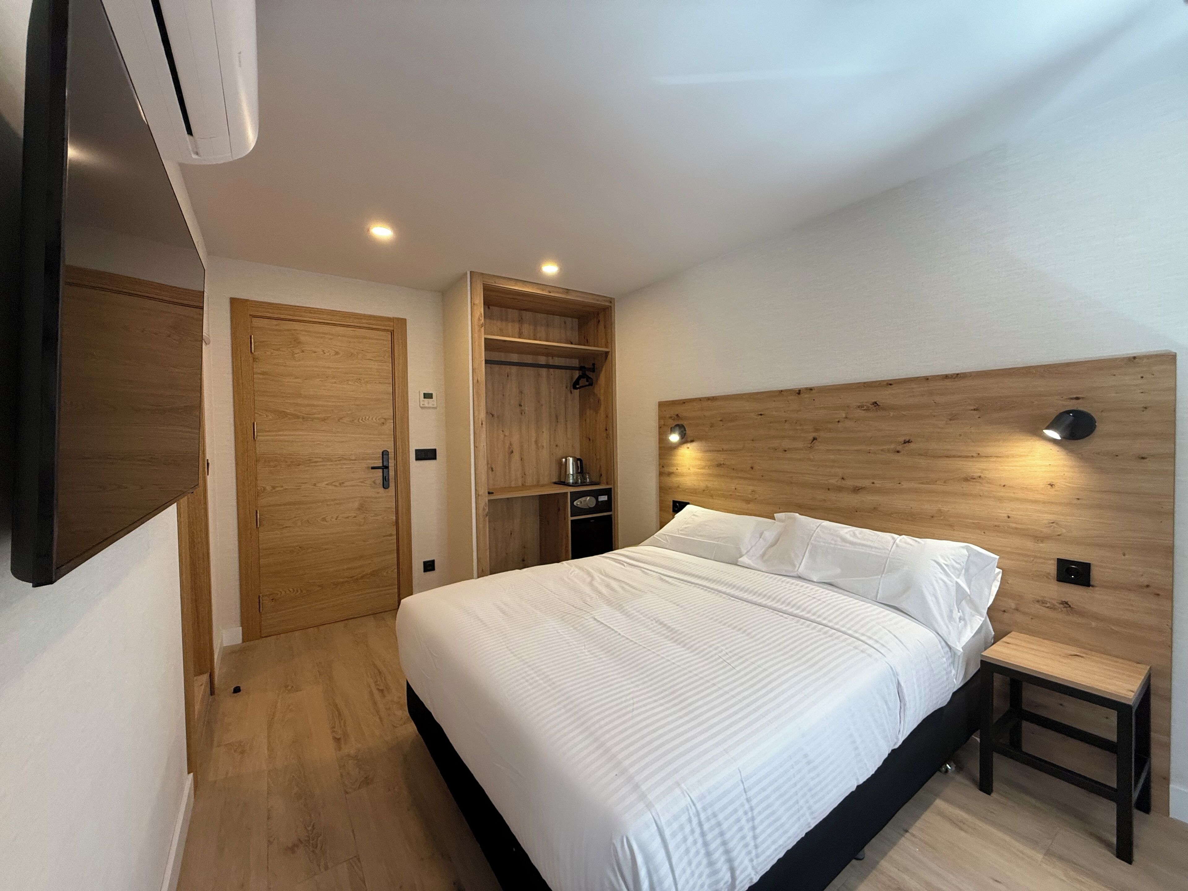 A bedroom with a wooden headboard, a bed with white linens, a wooden wardrobe, and a small wooden table.