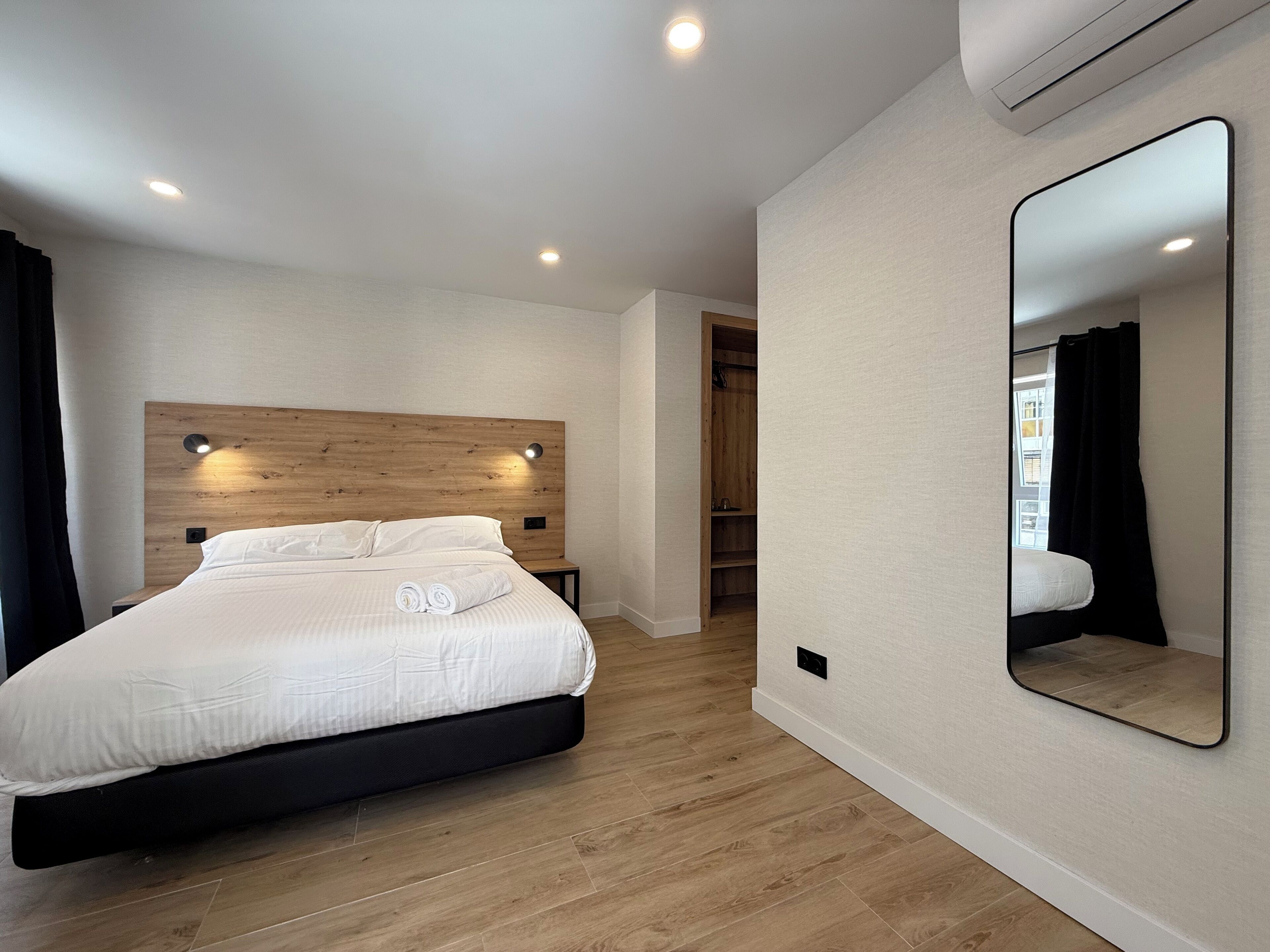 A modern bedroom with a wooden headboard, a large mirror, and a built-in wardrobe.