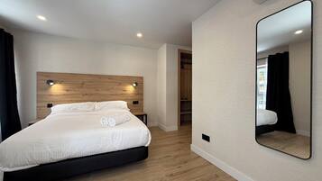 A modern bedroom with a wooden headboard, a large mirror, and a built-in wardrobe.