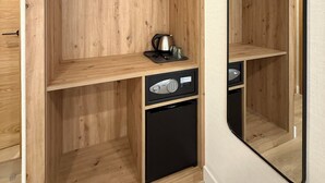 A wooden wardrobe with a mirrored closet door, a small shelf with a kettle, and a black appliance drawer.