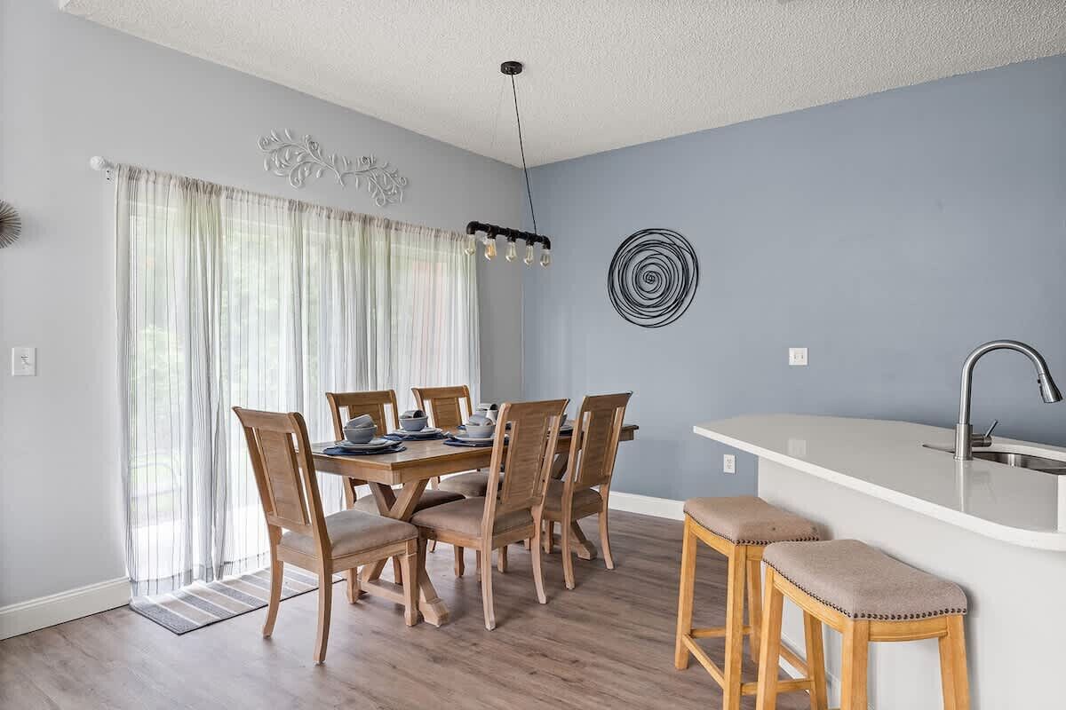 A dining area with a wooden table and chairs, a kitchen island with a sink, and a decorative wall piece.
