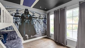 Un dormitorio con un mural inspirado en Star Wars, una cama litera y un ventanal con cortinas.