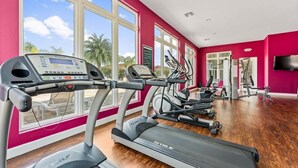 Un gimnasio con cintas de correr, elípticas y máquinas de pesas, ventanas amplias y una pared roja.