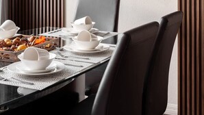 Un área de comedor con un espejo redondo, una lámpara con marco negro y una mesa dispuesta con vajilla y platos blancos.