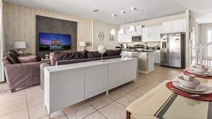 A modern living room with a sofa, a TV, and a dining area with a table set for two. - Disney Getaway! Private Pool & Themed Bedrooms. Book Now! #Solt429 (Orlando)