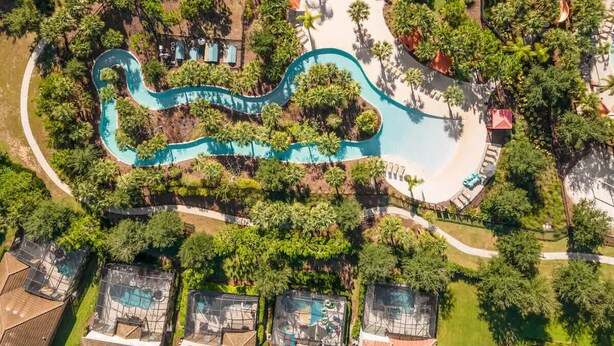 An aerial view of a resort with a winding pool, surrounded by lush greenery and palm trees. - Disney Getaway! Private Pool & Themed Bedrooms. Book Now! #Solt429 (Orlando)
