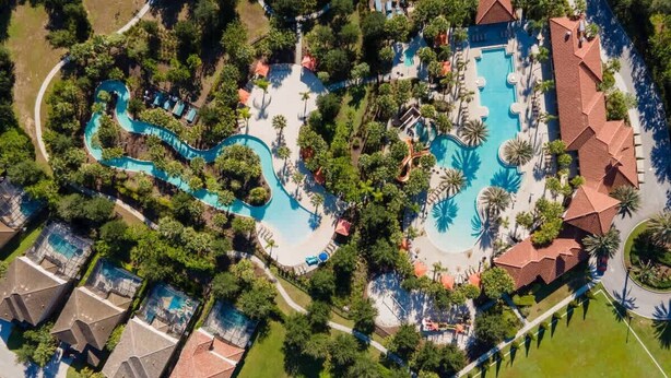 An aerial view of a resort with multiple swimming pools, a winding water slide, and lush landscaping.