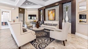 A spacious living room with a large sofa, armchairs, and a coffee table. There is a fireplace, a large painting, and a vase on the wall.