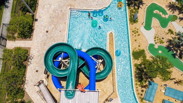 An aerial view of a water park with a large pool, multiple slides, and a green spiral water feature. - Disney Getaway! Private Pool & Themed Bedrooms. Book Now! #SLR506 (Orlando)