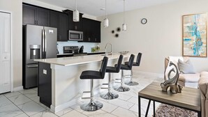 A modern kitchen with dark cabinets, a stainless steel refrigerator, a microwave, and a large island with bar stools. - Disney Getaway! Private Pool & Themed Bedrooms. Book Now! #SLR506 (Orlando)