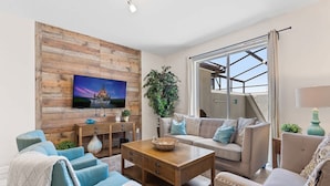 A living room with a wooden wall, a television, a sofa, and a coffee table. - Disney Getaway! Townhouse with Private Pool. Book Now! #SLR504 (Orlando)
