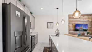 A modern kitchen with a large island, stainless steel appliances, pendant lighting, and a wooden accent wall with a TV. - Disney Getaway! Townhouse with Private Pool. Book Now! #SLR504 (Orlando)