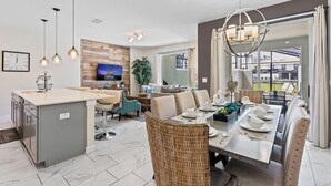 A modern kitchen with a central island, dining area with a table set for four, and a living area with a sofa and TV. - Disney Getaway! Townhouse with Private Pool. Book Now! #SLR504 (Orlando)