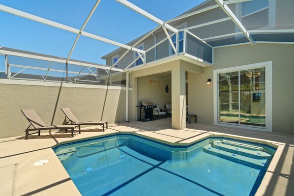 Une piscine avec des chaises longues, un patio couvert et un espace barbecue.