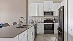 A modern kitchen with white cabinets, stainless steel appliances, and a grey countertop.