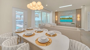 Un comedor moderno con una mesa blanca dispuesta para seis personas, rodeada de sillas blancas tapizadas.