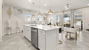 A modern kitchen with white cabinetry, a central island, pendant lighting, and a dining area with white chairs. - Last Minute Disney Getaway! Private Pool & Comfortable Bedrooms. Book Now! #147409 (Orlando)