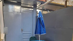 Un piccolo spazio all'aperto con un tavolo e due sedie blu, un ombrellone blu e erba sintetica verde.