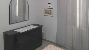 Una camera da letto con una cassettiera nera, uno specchio, un condizionatore d'aria, un quadro incorniciato e tende leggere.