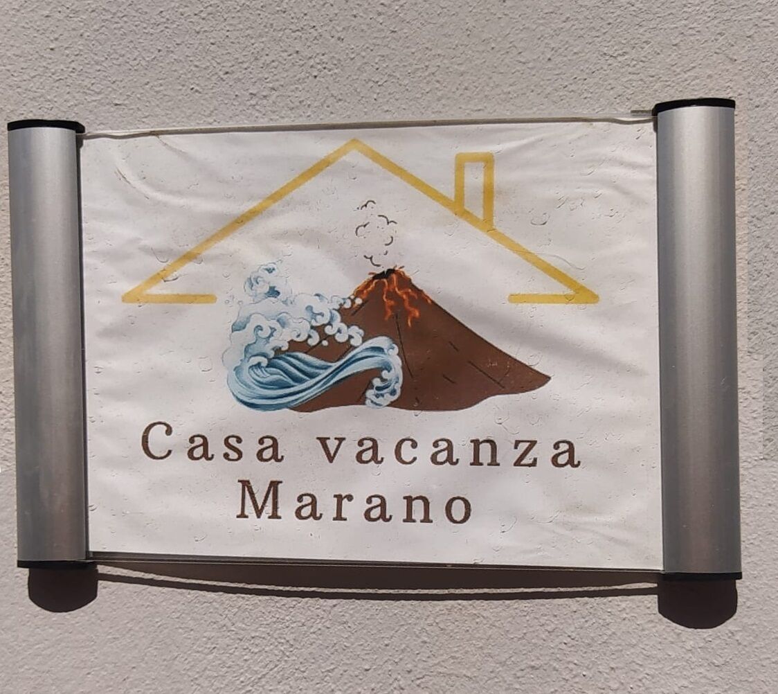 A sign for 'Casa vacanza Marano' featuring a house and a volcano with waves.