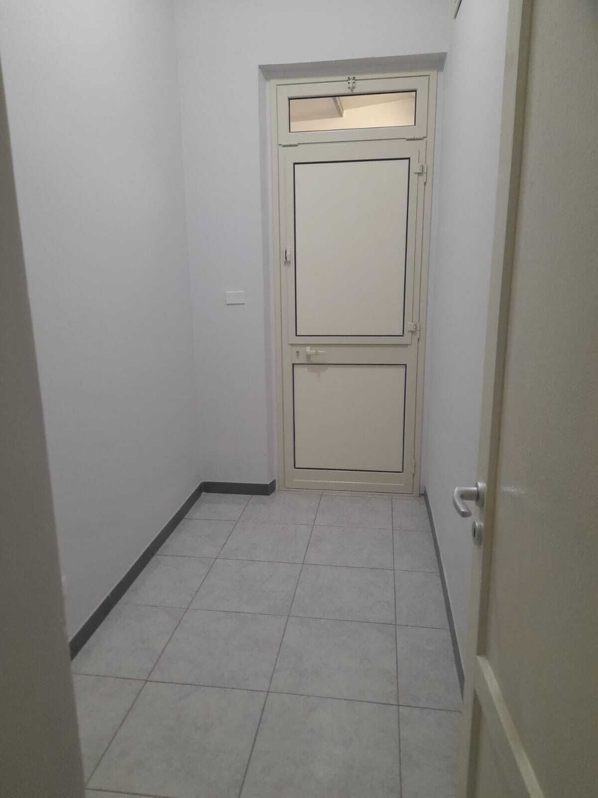 A narrow hallway with a double door, tiled floor, and a light switch on the wall.