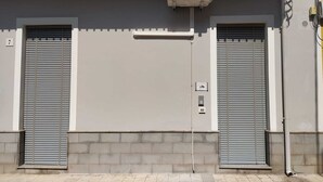 Facciata di un edificio con due persiane avvolgibili chiuse e un piccolo condizionatore d'aria montato sopra.