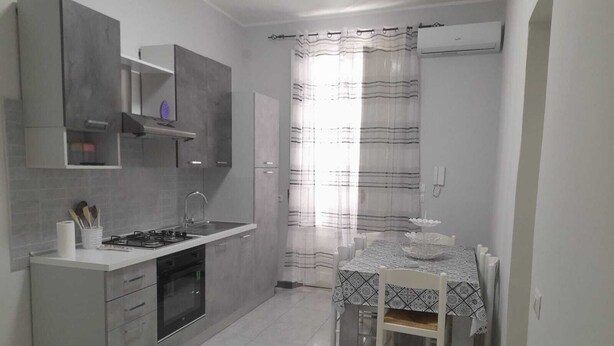 Una cucina moderna con mobili grigi, forno integrato e zona pranzo con tavolo e sedie.