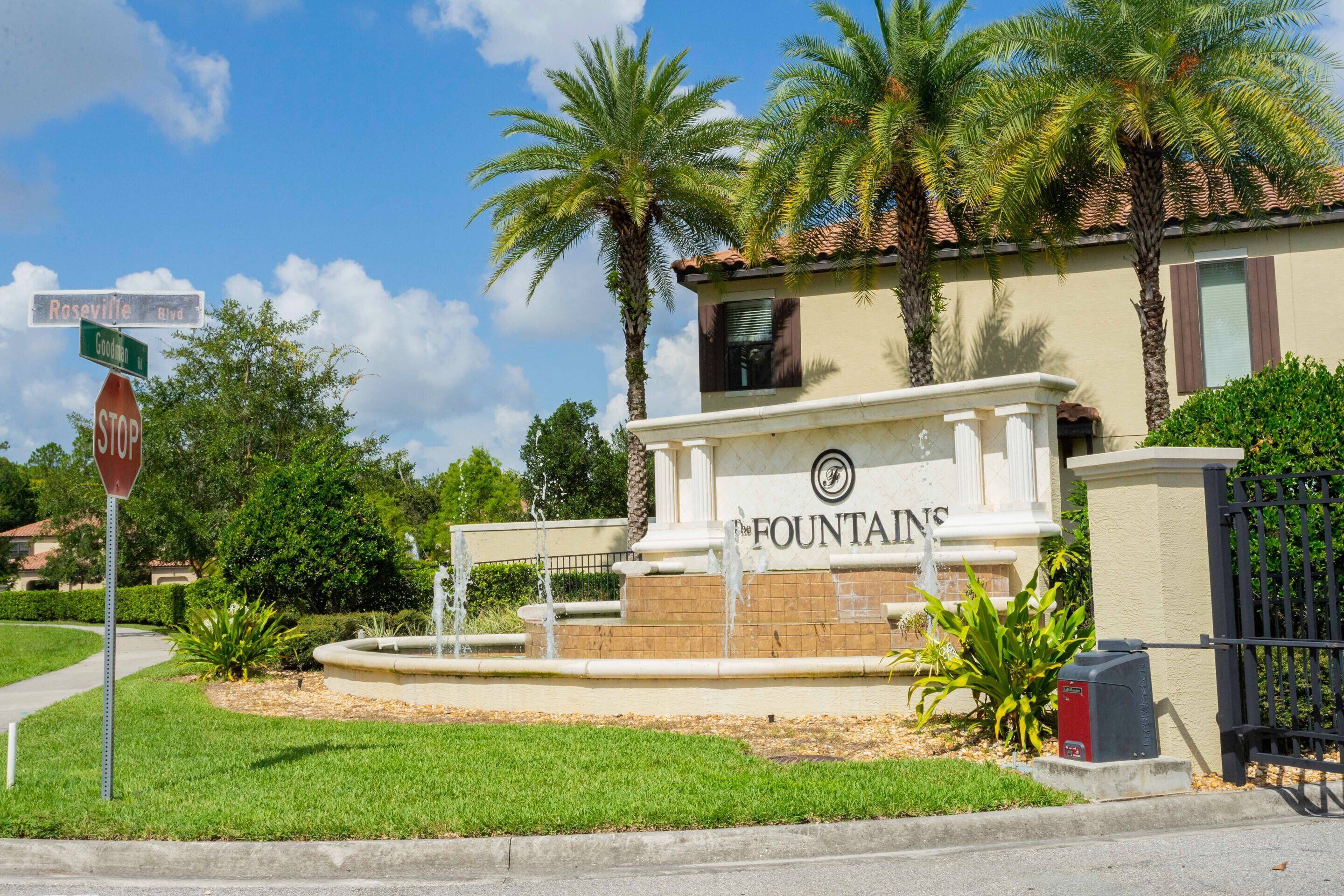 Un bâtiment portant l’inscription « The Fountains », avec un panneau de signalisation indiquant un arrêt, des palmiers et une fontaine devant.