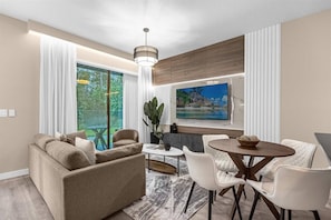 A modern living room with a sofa, dining table, chairs, a TV, and a large window with curtains.