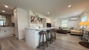A modern kitchen with a central island, bar stools, a dining area with a sofa, and a living room with a lamp. - 3BR Single Family with Pool in Naples, less than 2 miles to Beach! (Naples)