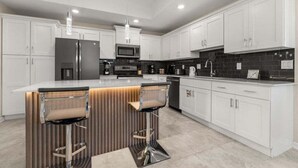 Una cocina moderna con armarios blancos, electrodomésticos de acero inoxidable y una isla central con taburetes de bar.