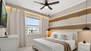 Un dormitorio moderno con una cama, mesitas de noche, un ventilador de techo y una ventana con cortinas.