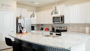 A modern kitchen with white cabinets, granite countertops, stainless steel appliances, and pendant lighting.